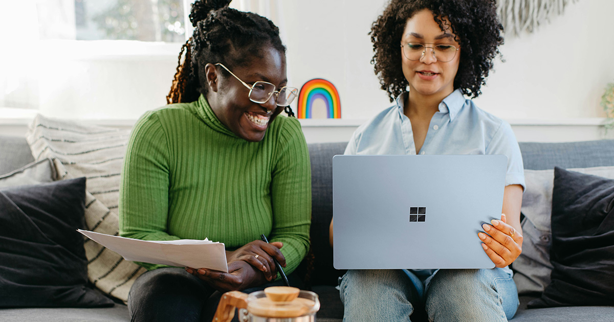 Two women sitting on the couch while looking at a laptop