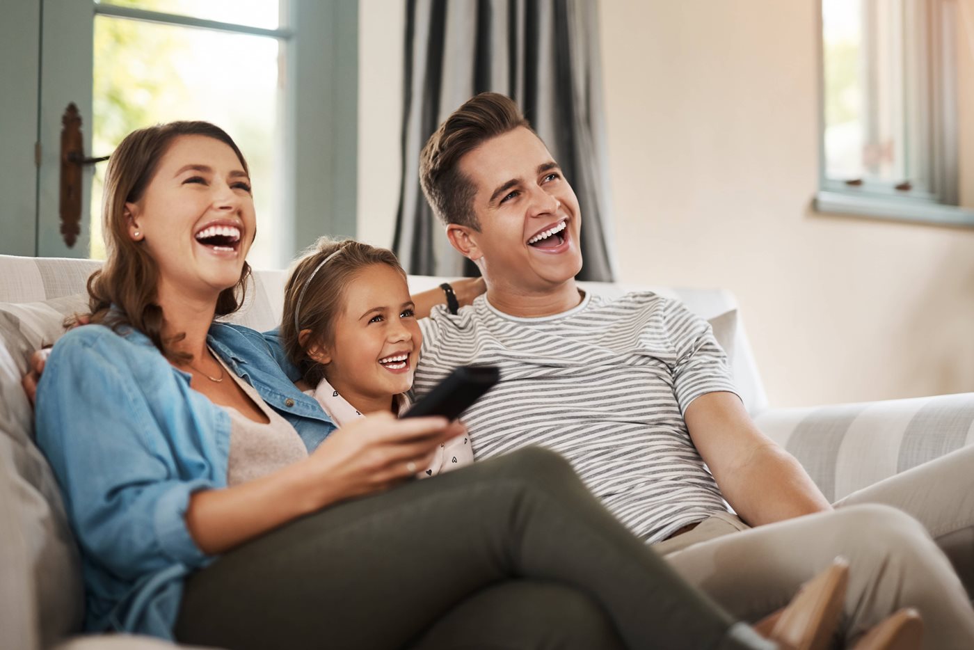 A small military family laugh together while watching TV on the couch