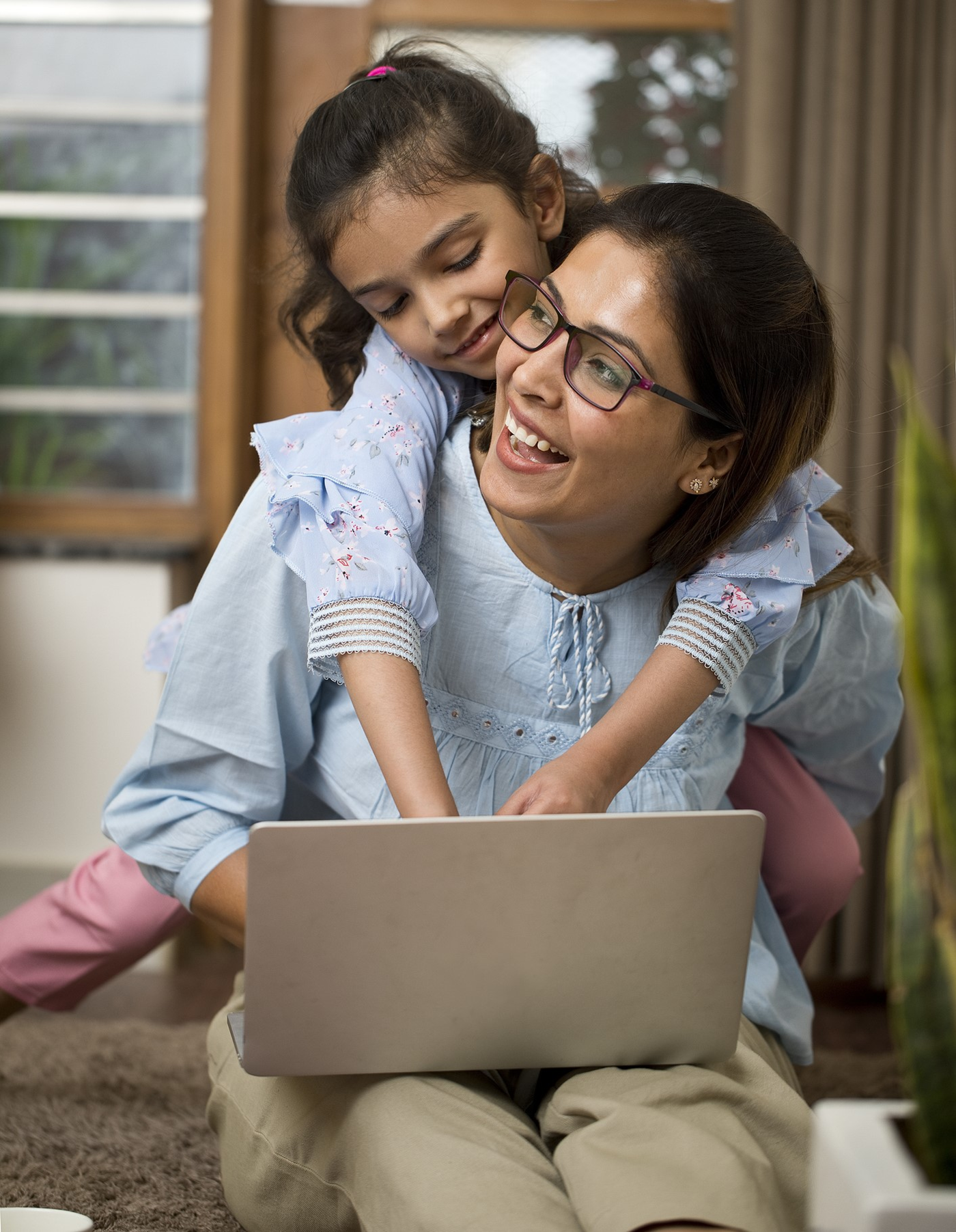 A military spouse laughs while her young daughter types on her laptop over her shoulders