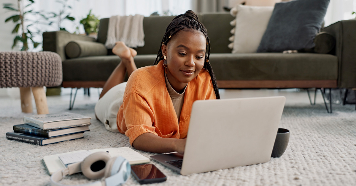 A young woman lies on the floor while working on her laptop