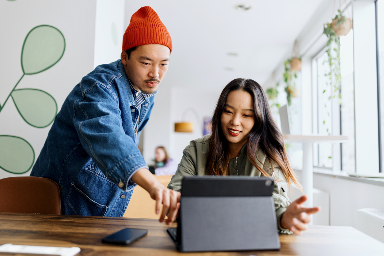 Two people work together at a table, looking at a tablet. One points at the screen while the other smiles, possibly running a Hargray Internet speed test in a bright, modern office or cafe.