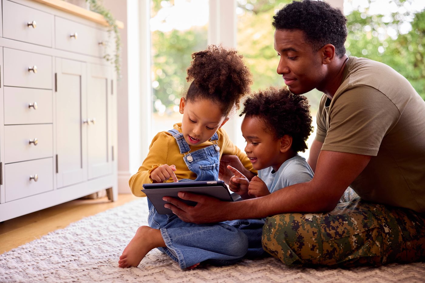 A military dad in camo pants helps his children on their iPad
