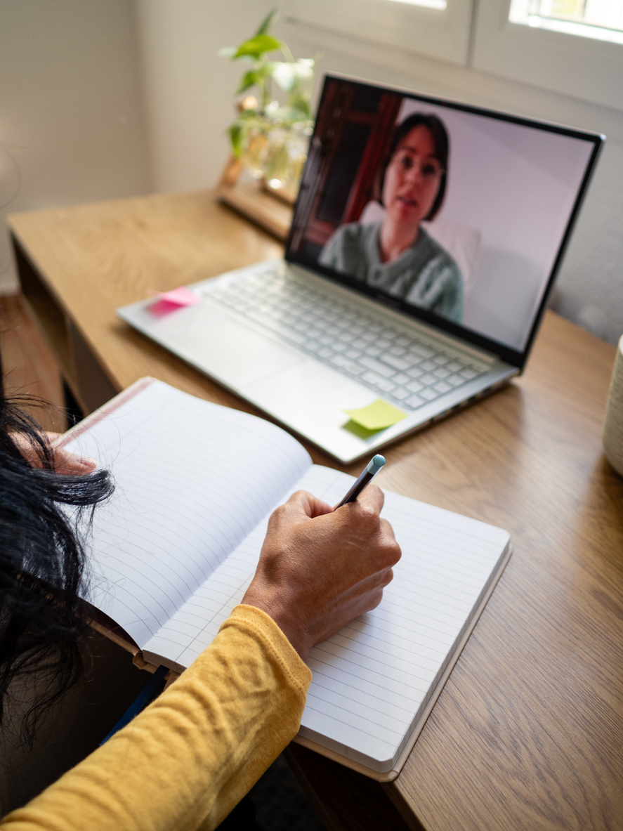 woman coaching online while taking notes at home.