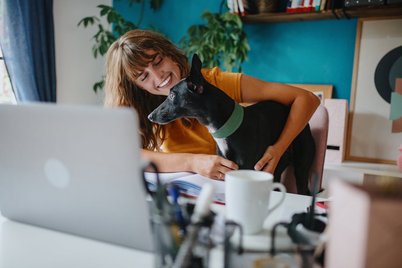 A young woman smiles at her dog on her lap while they sit at her laptop using Spectrum Internet