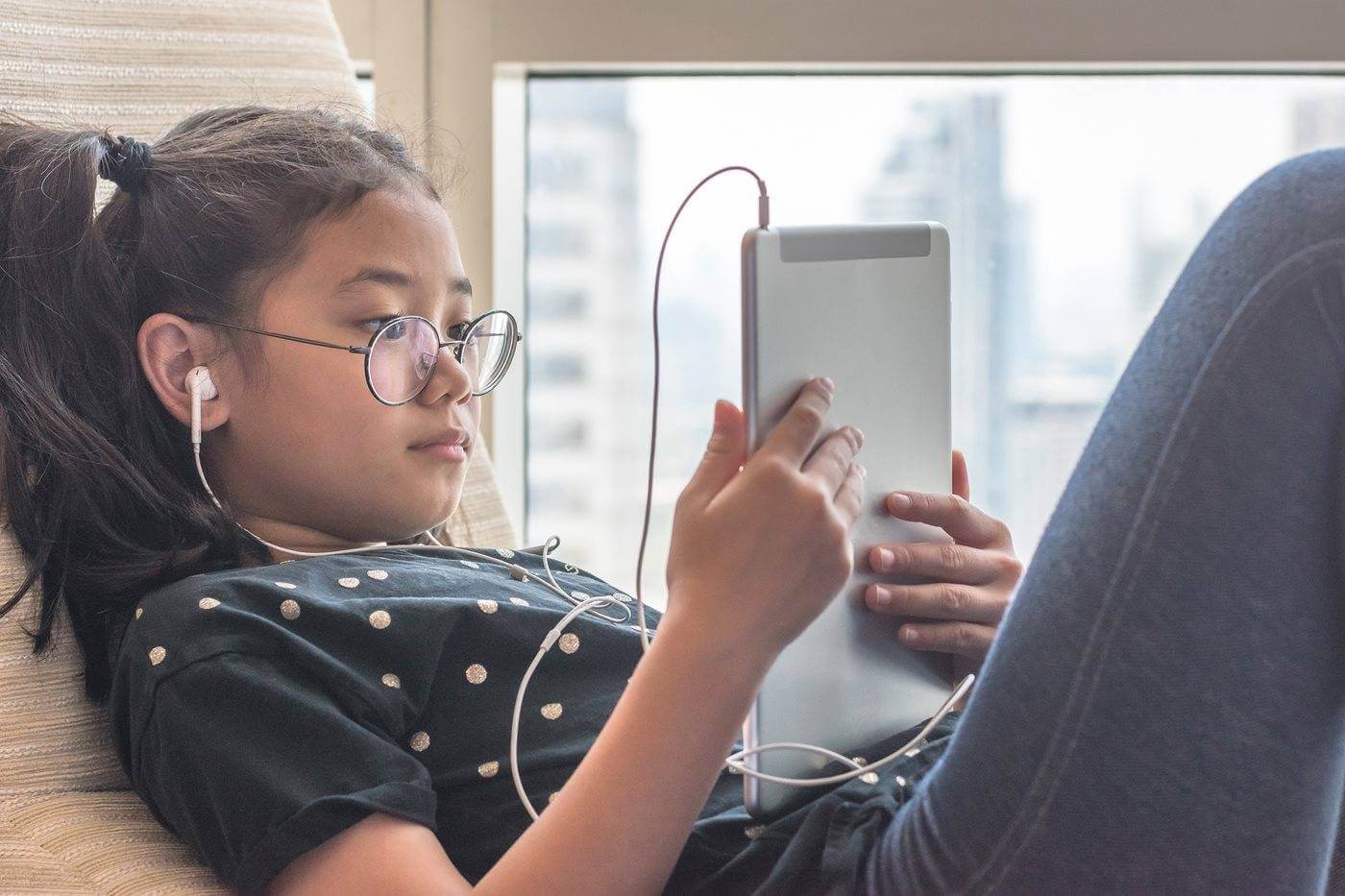 A young girl with pigtails and glasses plays on her iPad