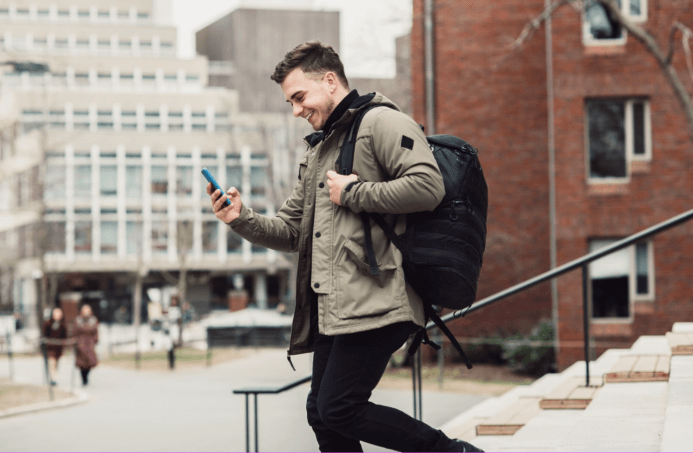 Man with a backpack walks while smiling at his smartphone