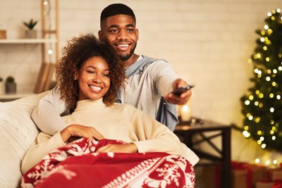 A couple snuggles on the couch surrounded by Christmas decorations while streaming holiday movies after using SmartMove’s tool to find where to watch the best holiday movies.