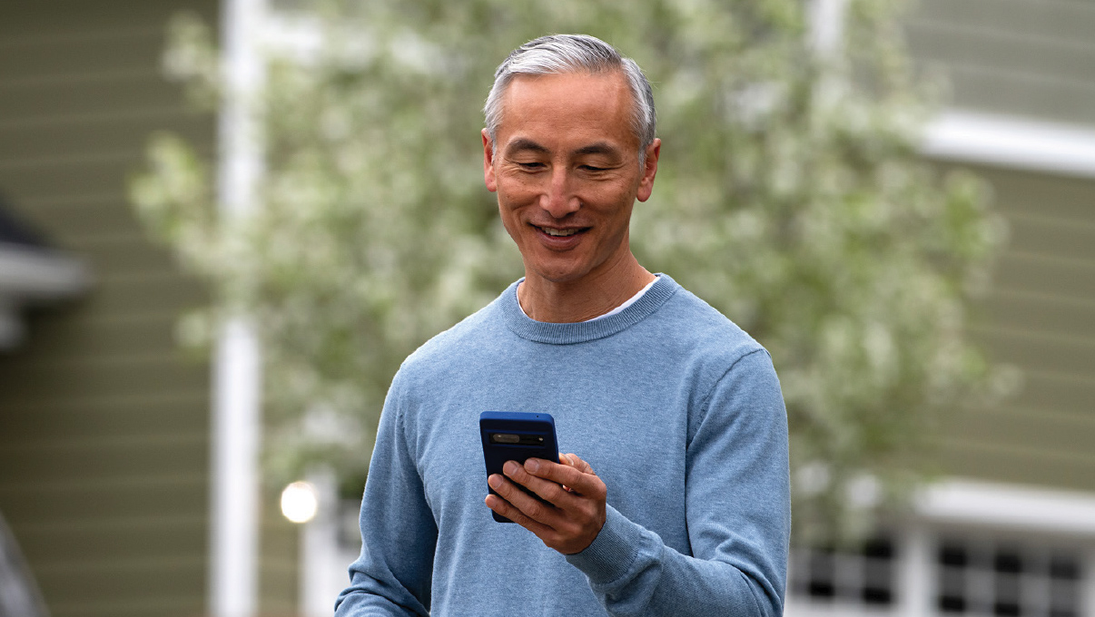 A man smiling down at his phone while using Optimum Mobile