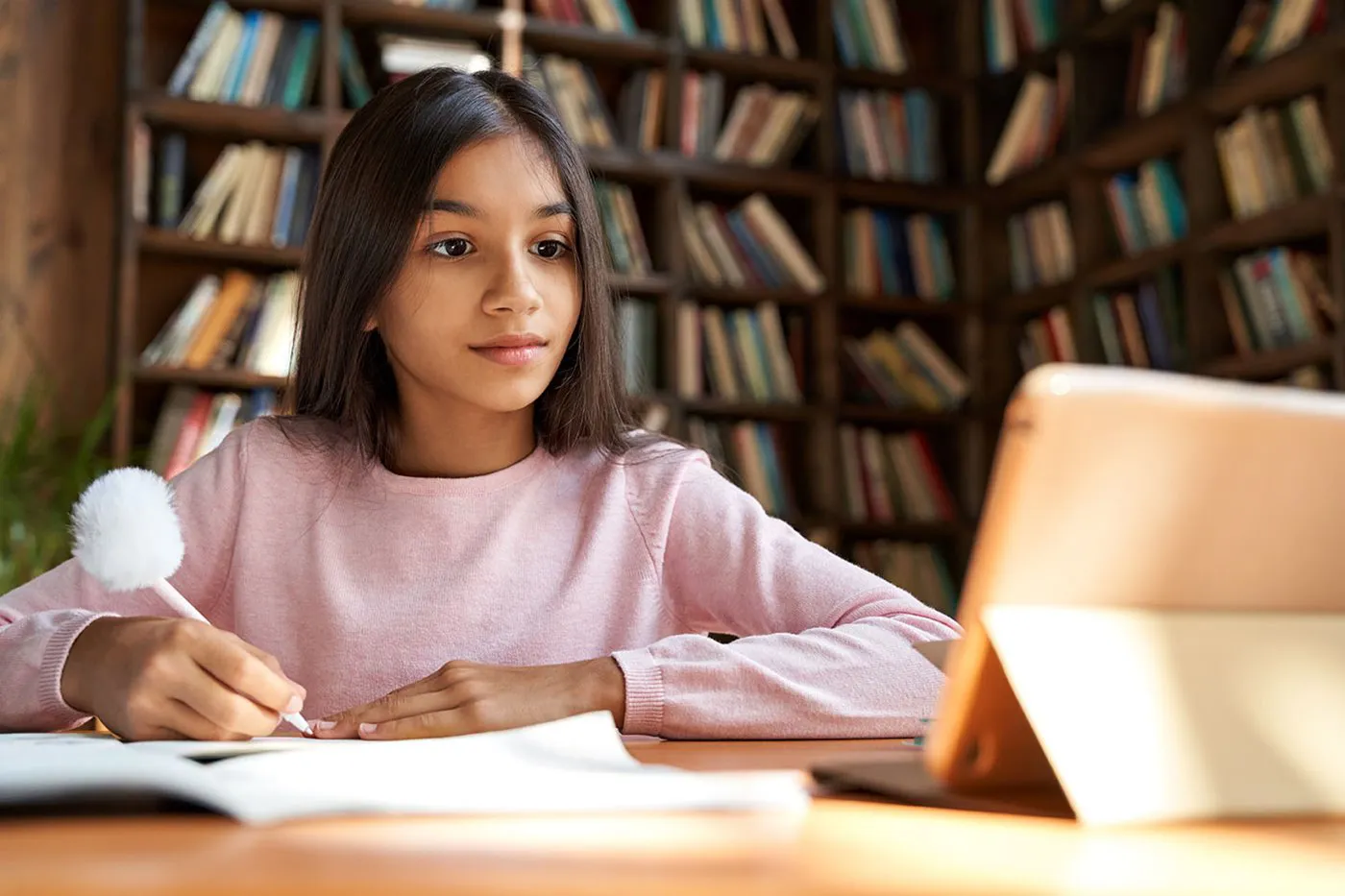 A young girl looks at her iPad while writing notes during e-learning