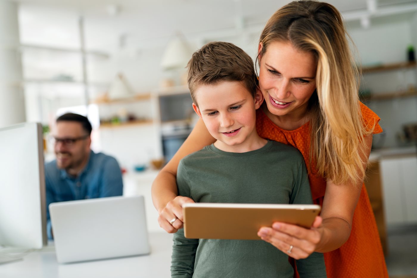 A mom and son look at an iPad together, while a dad works on his laptop in the background thanks to Fidelity Internet