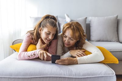 A mother and daughter sit on a couch together while using the Best Mobile Family Plans available