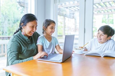 A Native American family smiles together while using a laptop connected to the Internet through the Affordable Connectivity Program offered to rural and tribal lands.
