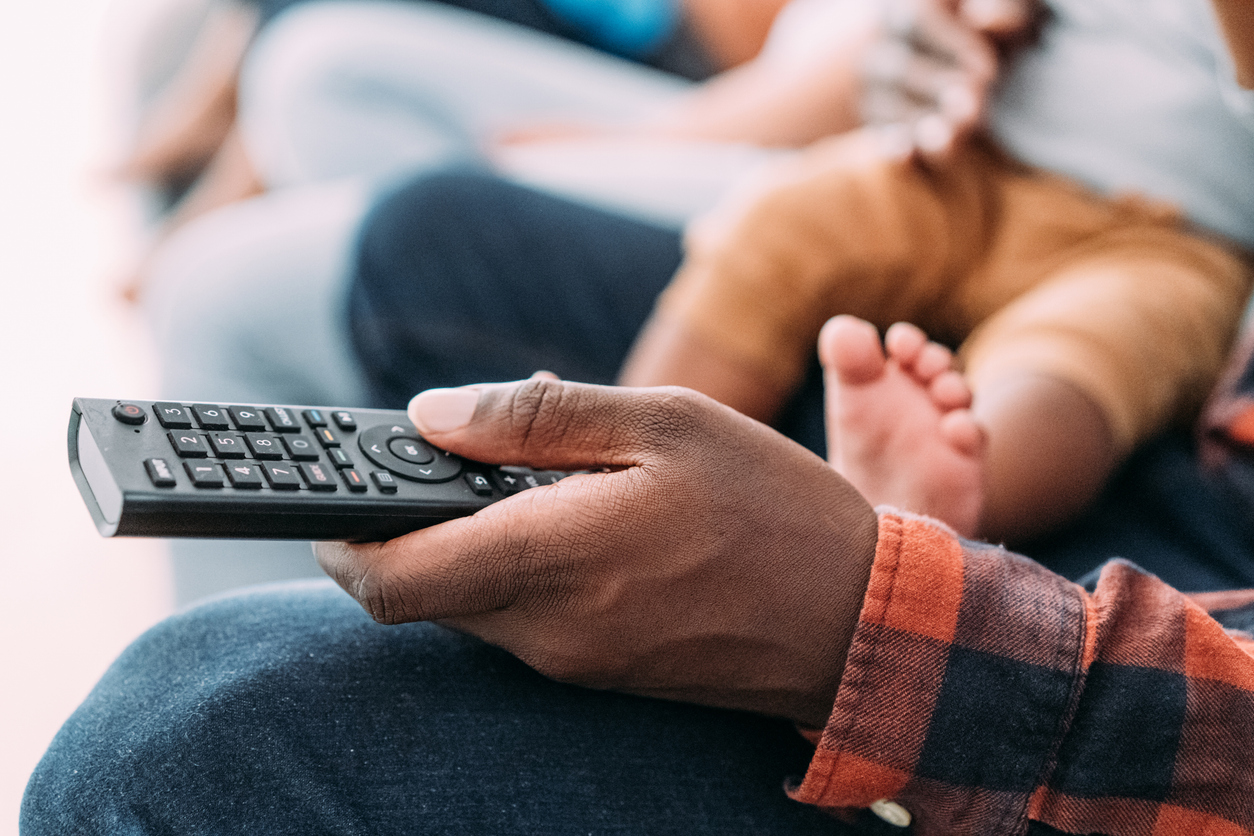 A person holding a television remote while sitting with a baby.