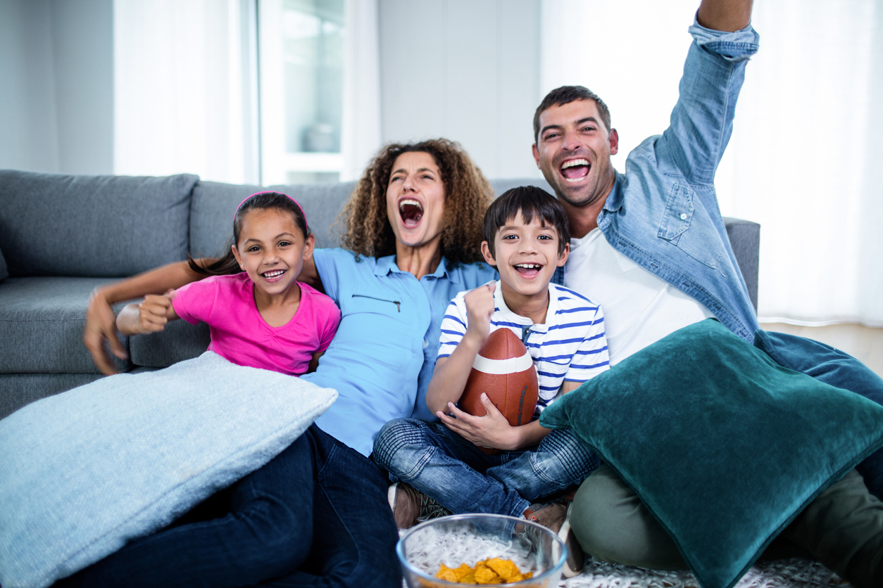 A family cheers while sitting on their couch watching sports