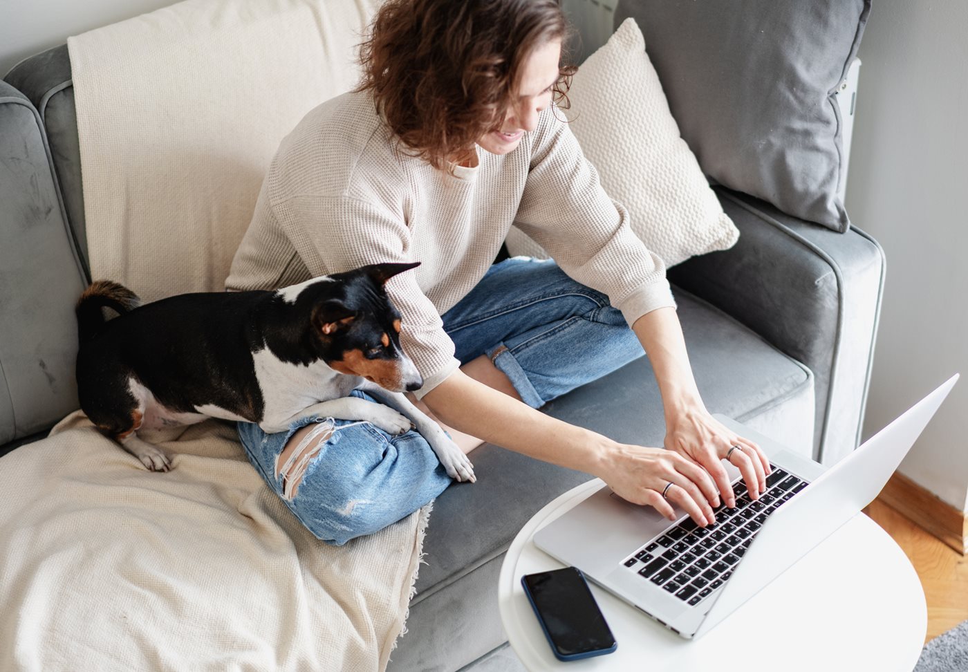 Aerial view of a woman sitting on the couch by her dog while working on her laptop powered by Fidelity Internet