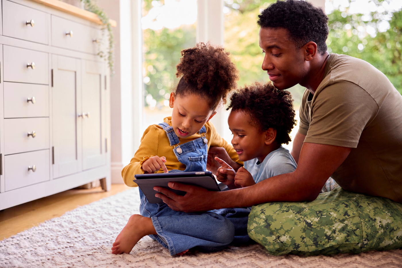 A military dad in camo pants helps his children on their iPad