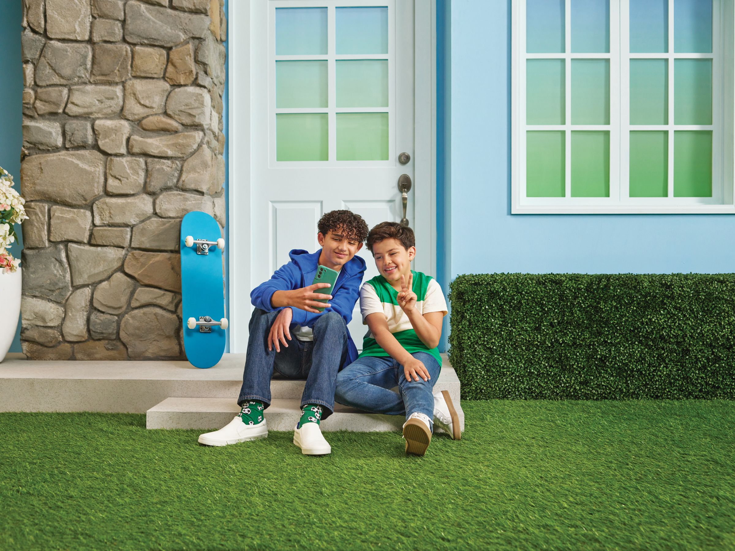 Two happy boys sit in a yard next to their skateboards while on their smartphones powered by Cox Mobile