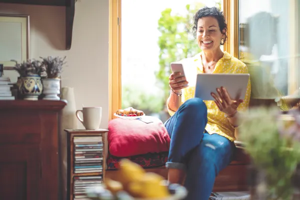 A woman sits in a window seat while holding her laptop and cell phone