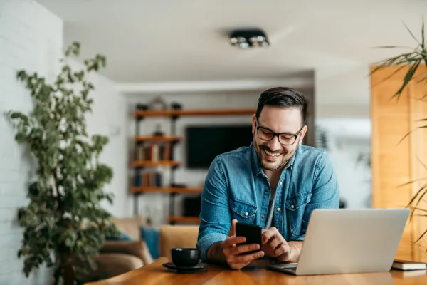 A young professional man smiles while looking at his laptop in his home office