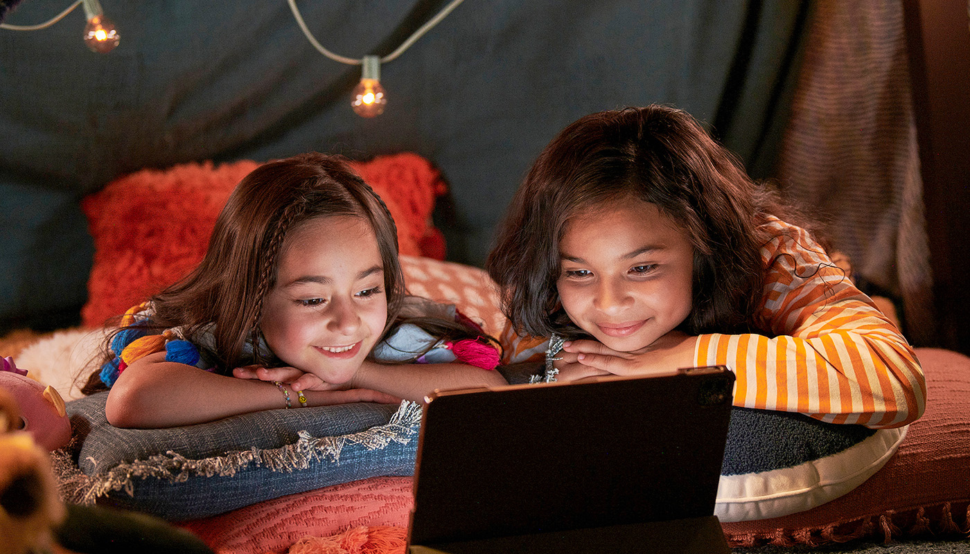 Two young girls smile at a laptop powered by Optimum Internet