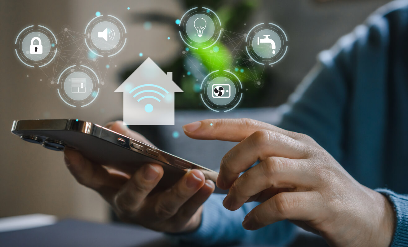 A hand holding a smart phone up with smart home icons illuminating from it