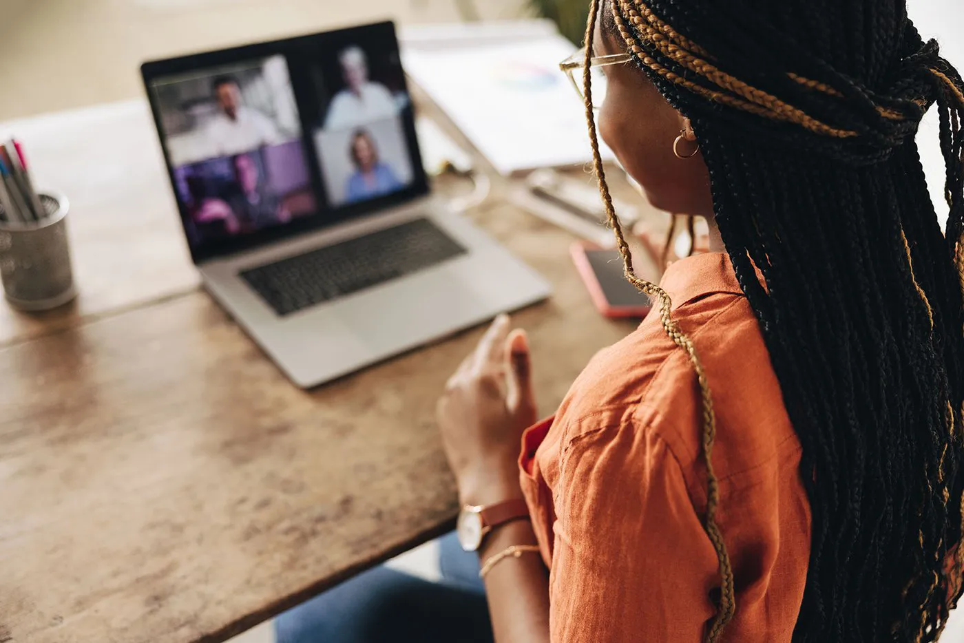 A young professional woman looks at her laptop while on a video call with coworkers