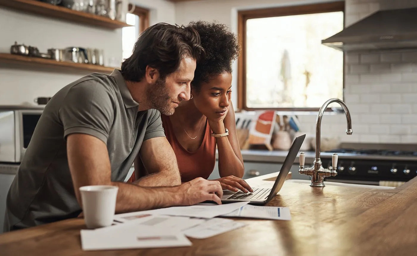 A young couple lean on a kitchen counter while testing their Optimum speed test on their laptop