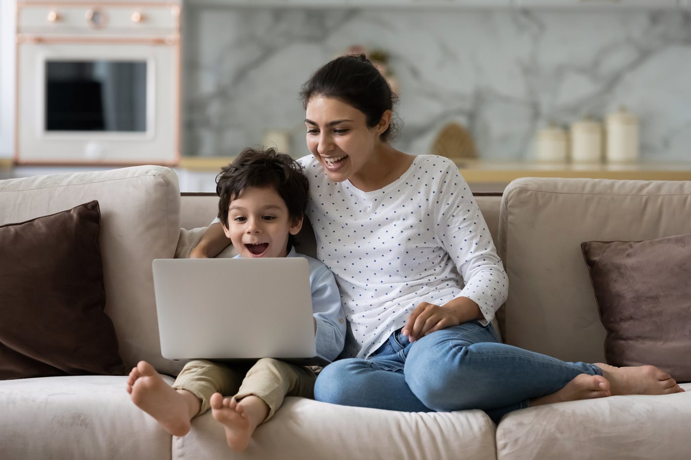 A mom and son sit together on a couch while looking at a laptop exploring Xfinity services