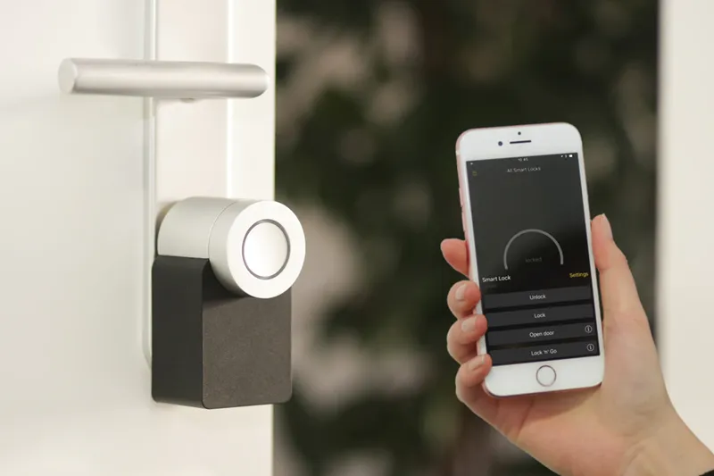 A hand holding a smart phone up next to a smart lock on a door