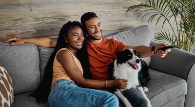 A couple and their dog happily sitting on their sofa while browsing the best streaming packages.