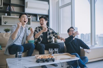 Three male friends celebrate a victory while streaming an NFL game in an apartment with a city skyline in the background.