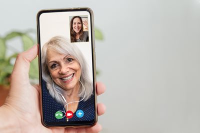 A phone screen shows a happy older woman smiling as she uses a video calling device to FaceTime her daughter.