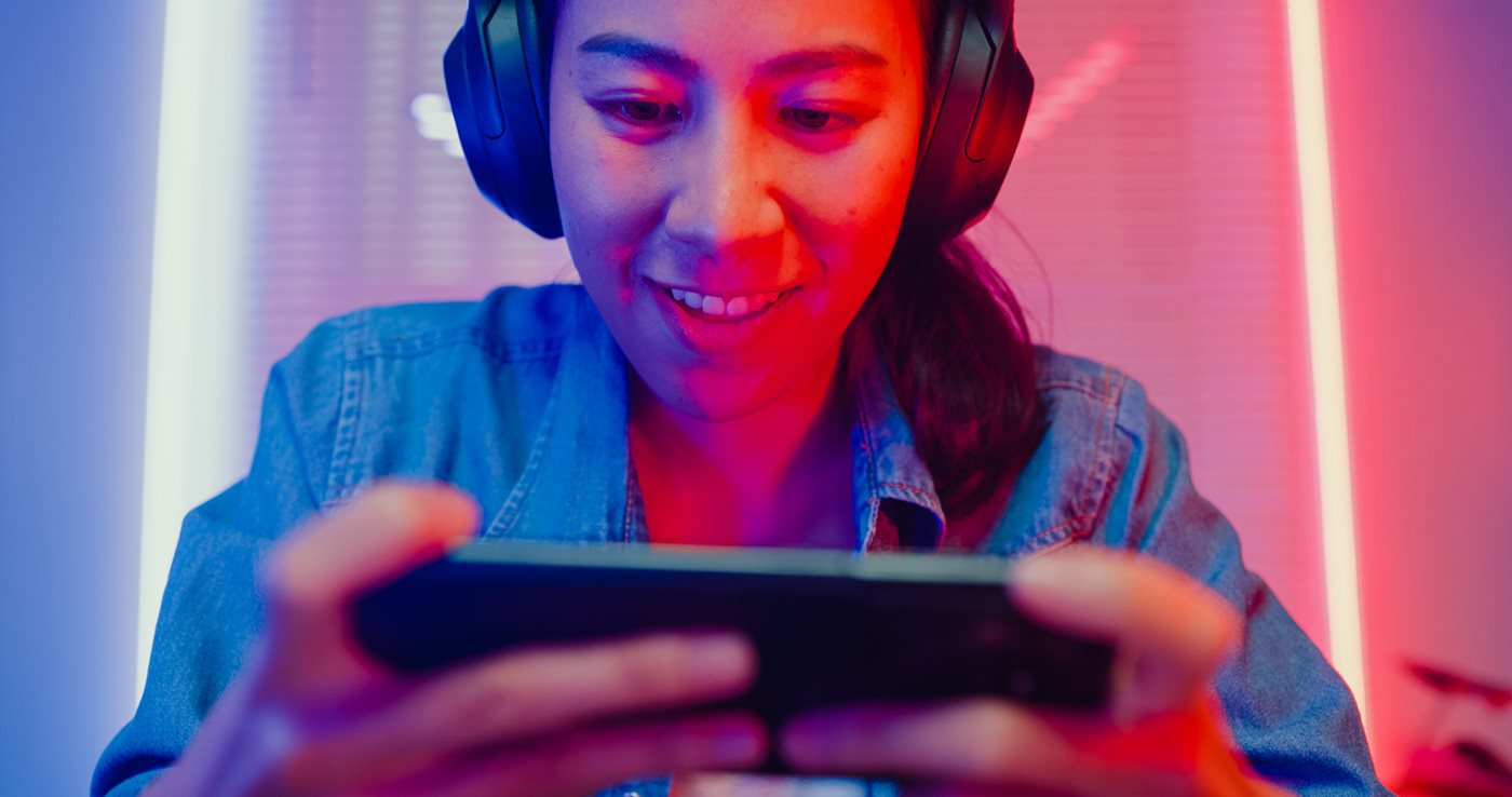 A young woman games on her phone while wearing headphones