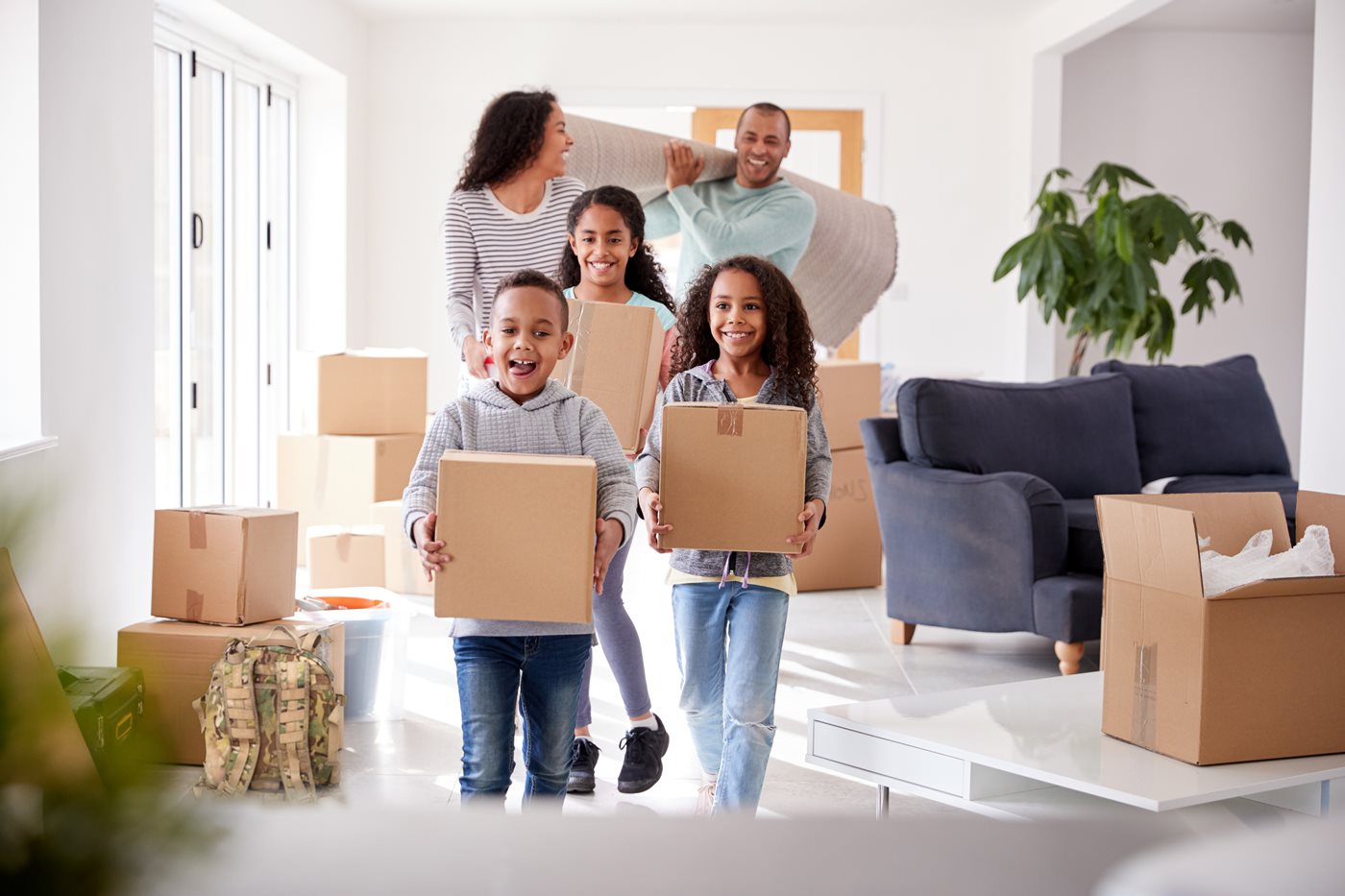 A military family carries moving boxes into their new home after a PCS