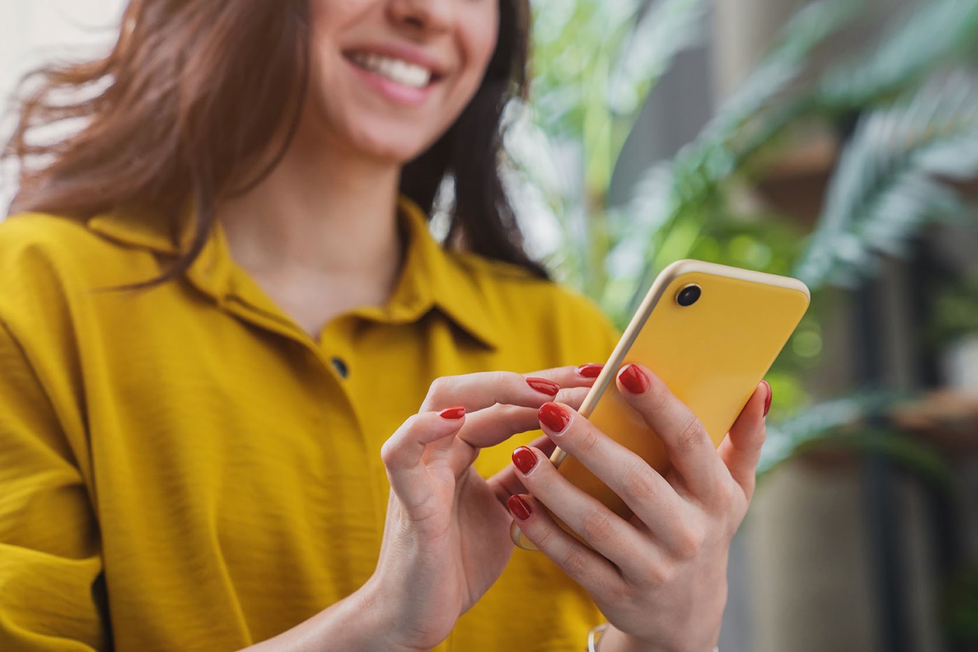 A woman in yellow smiles at the smartphone in her hands