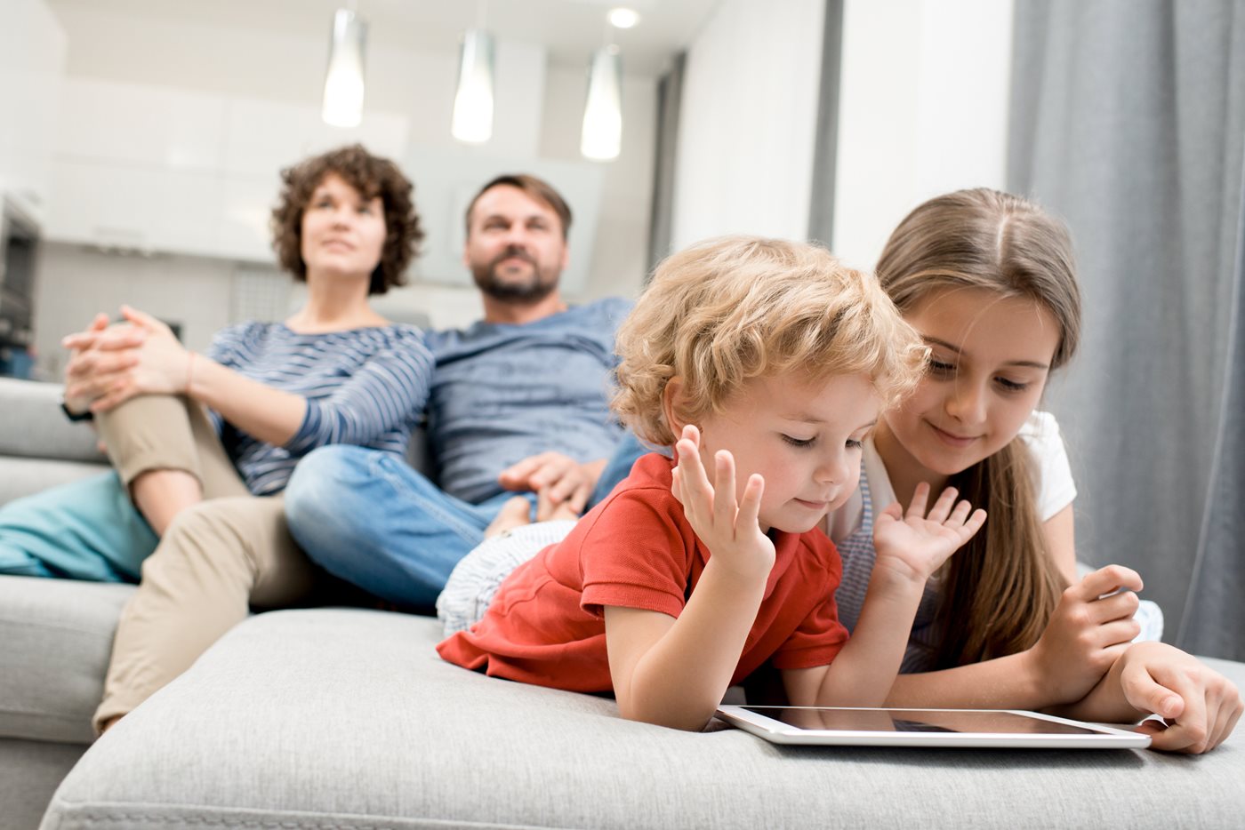 A young brother and sister play on an iPad while their parents watch TV, both powered by Sparklight