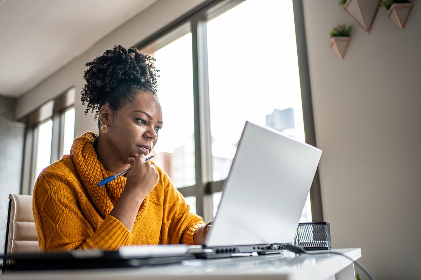 A woman in an orange sweater sits at her laptop while exploring the benefits MCTV Internet, TV and phone packages