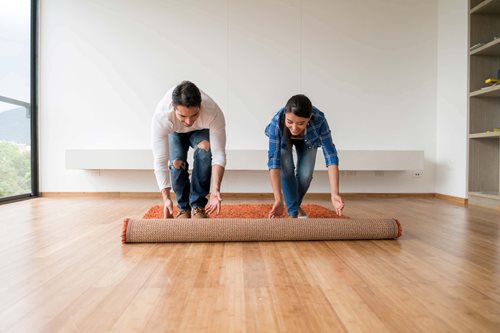 A young couple unroll a rug together while moving into their new home