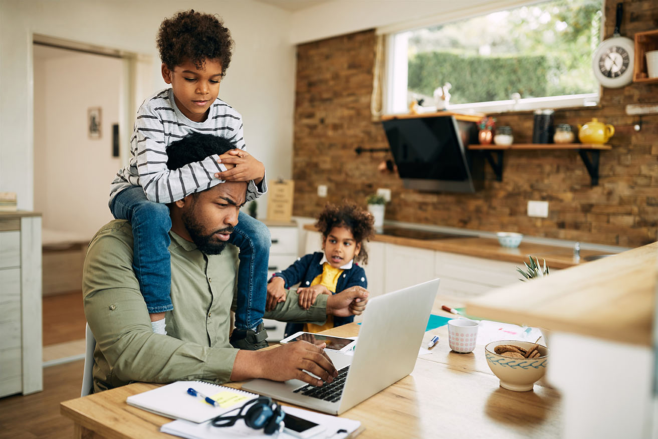 A father works on his computer at home while his young kids ask to play