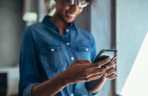 A woman smiles while looking down at her smartphone