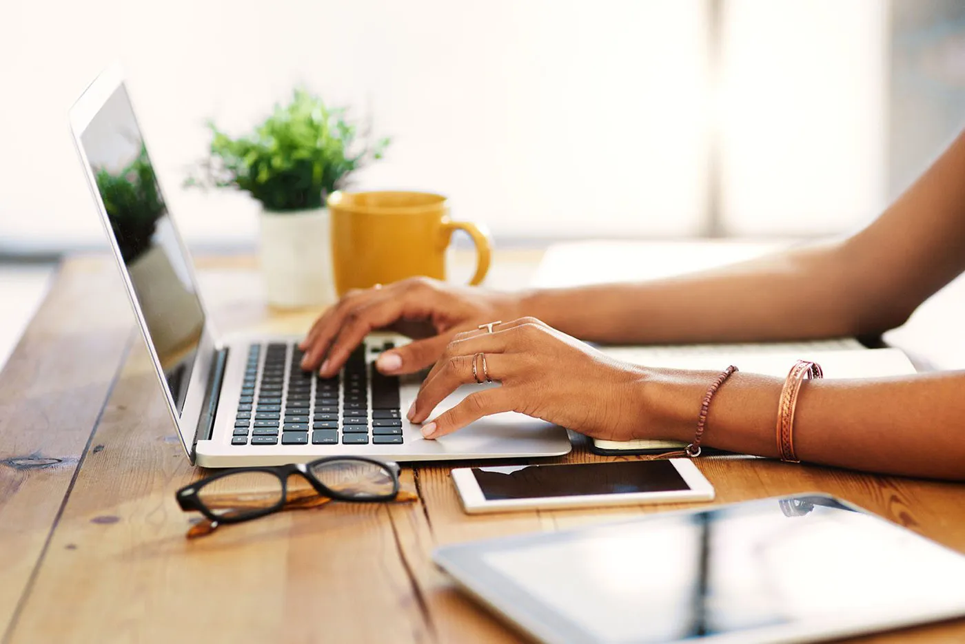 A woman's hands typing on a laptop while sitting at a wooden table