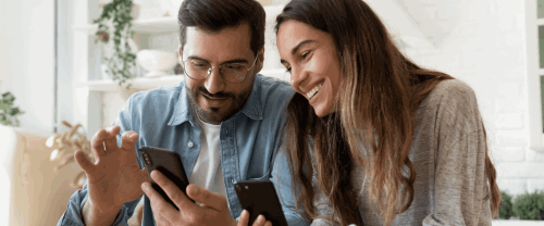 A young man and women smile while looking at their Smartphones