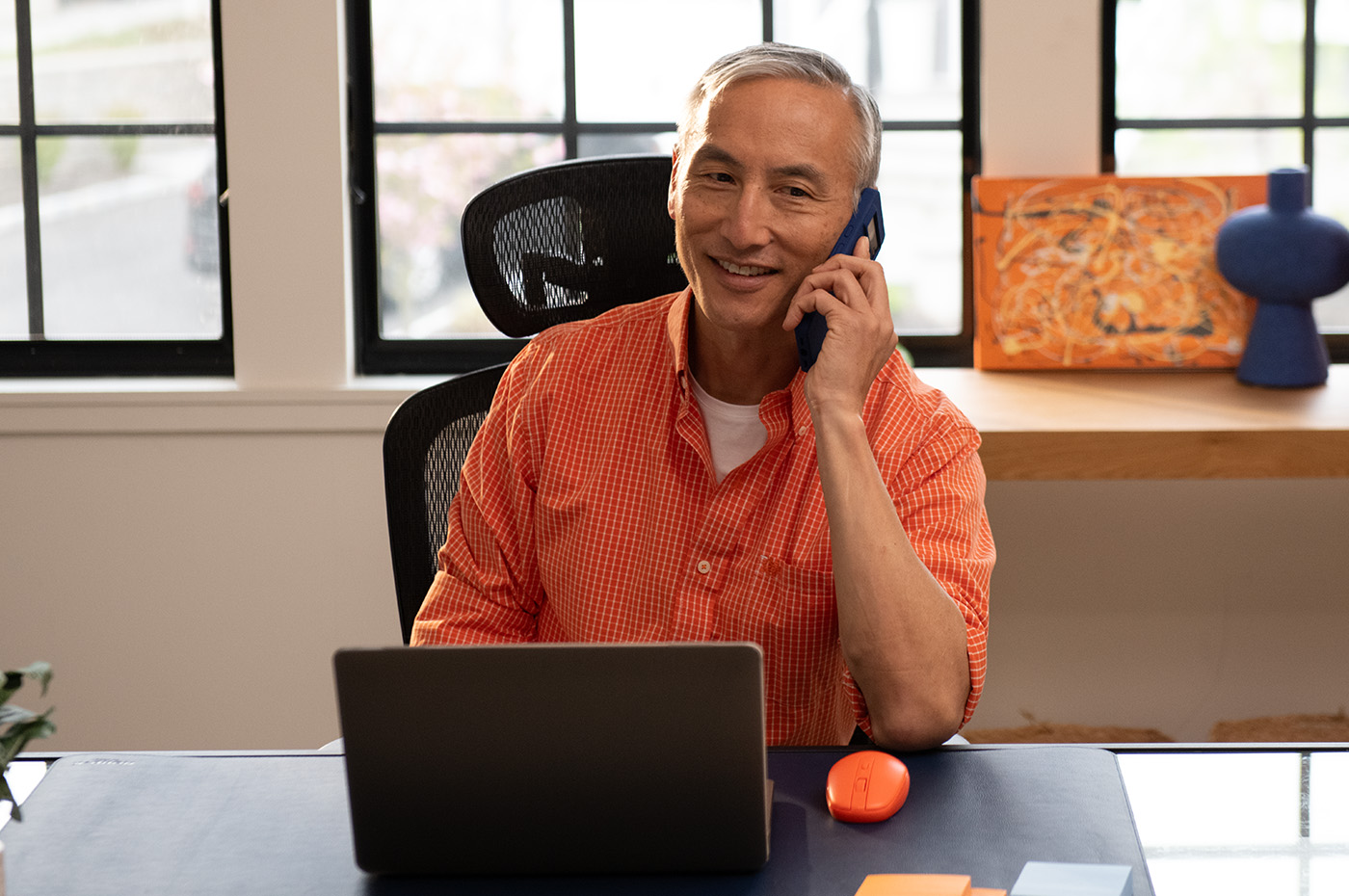 A man sits at a desk on his laptop while on the phone, with both devices being powered by Optimum