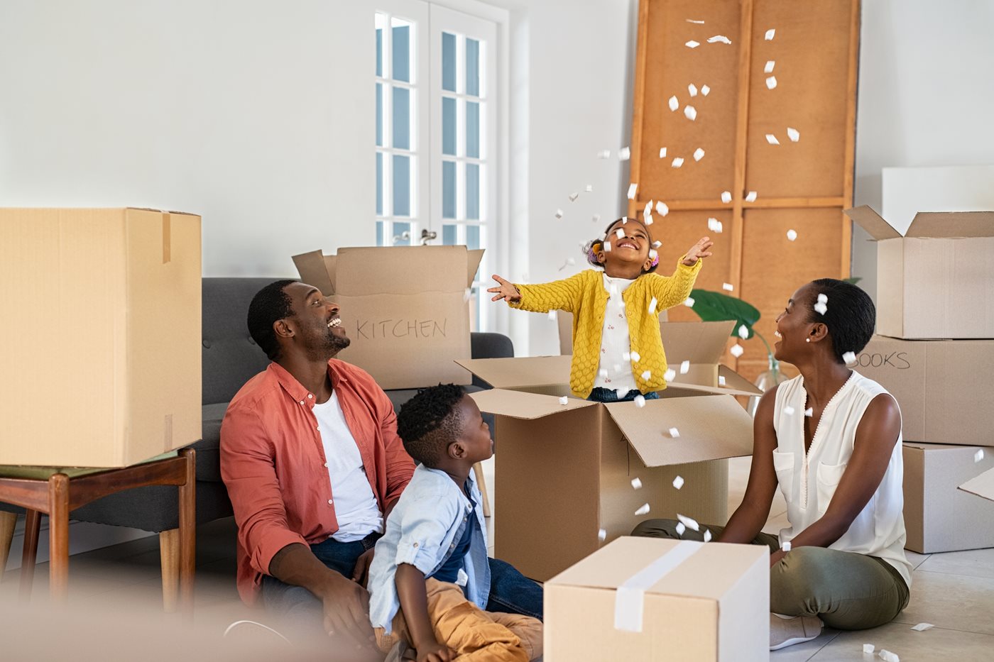 A dad, mom and son laugh while sitting on the floor of their new home surrounded by moving boxes