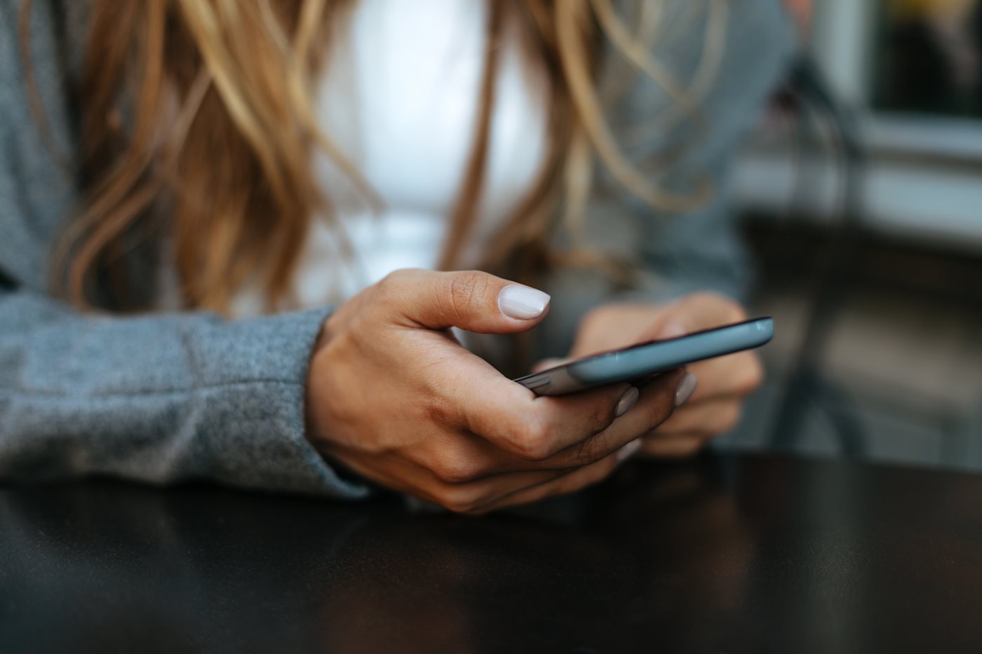 A mobile phone held by the hands of a woman with white nail polish and brown hair