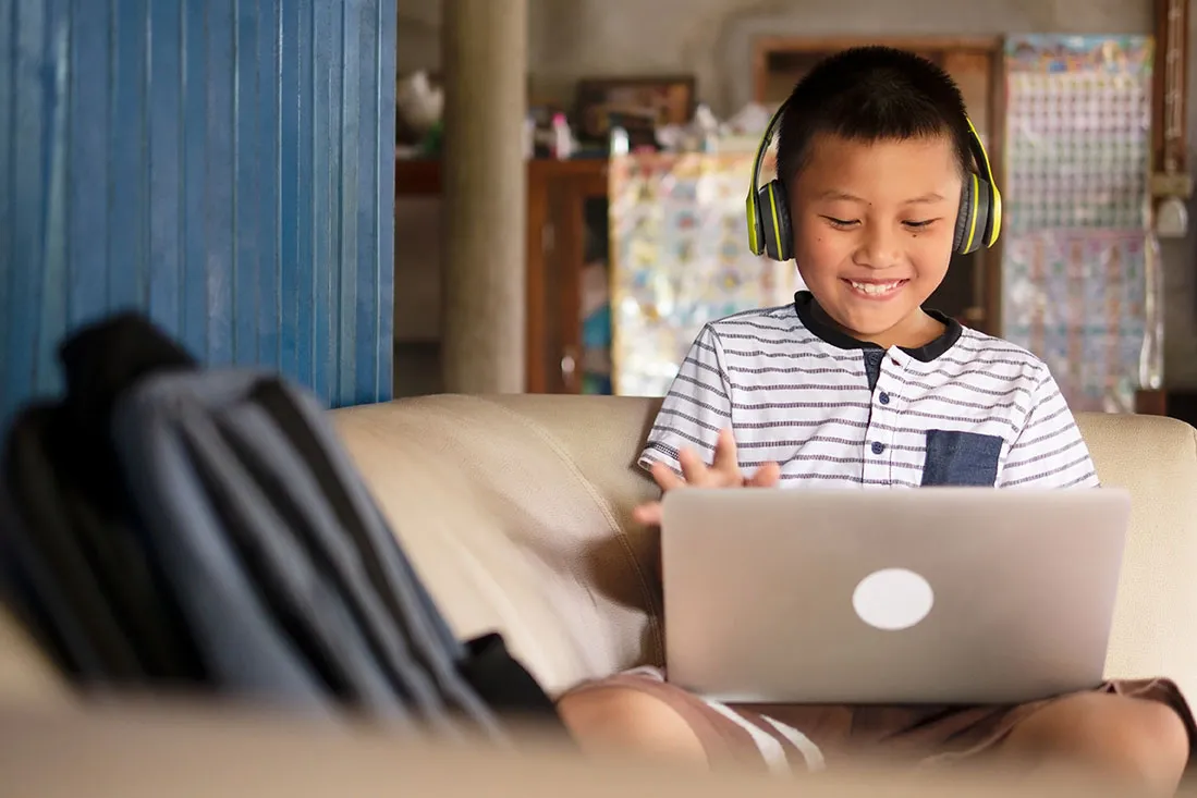 A young boy wears headphones and does schoolwork on his laptop