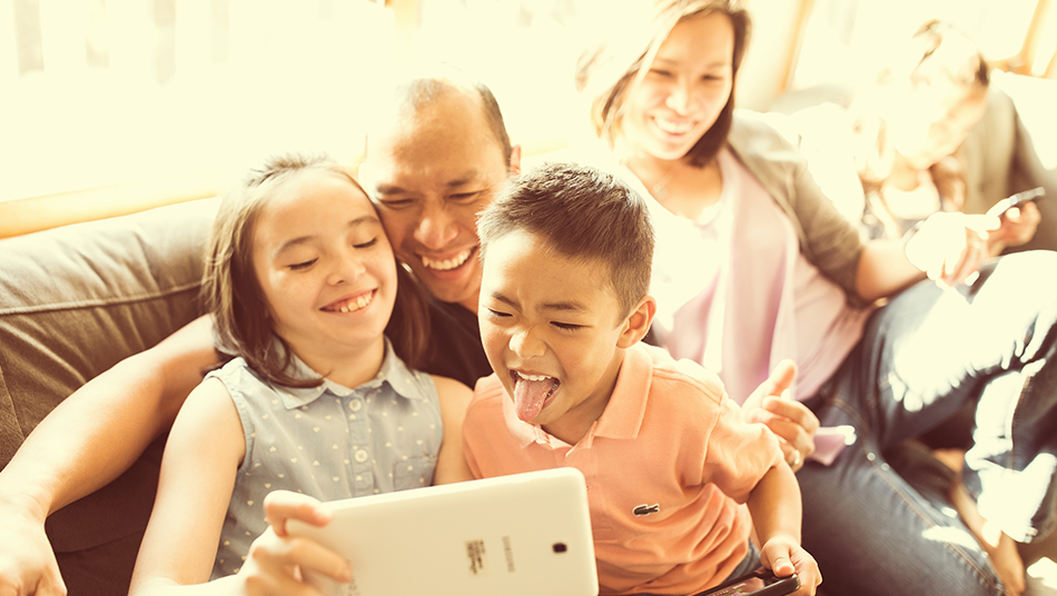 Two kids hold an iPad in front of themselves and their parents to take a family selfie