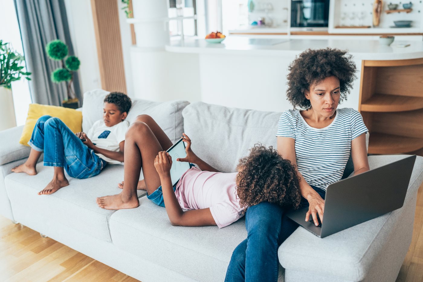 Una madre trabaja en su computadora portátil mientras sus hijos se sientan a su lado con sus iPads