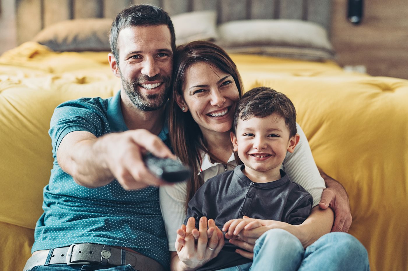 A mother and son snuggle as a father points a remote control at his TV powered by MCTV