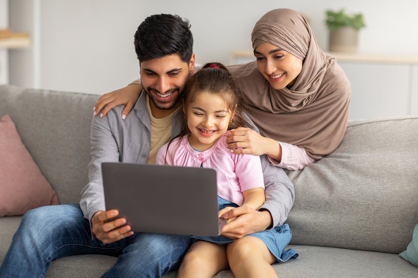 A mom leans over her husband and son's shoulders while they smile at their laptop